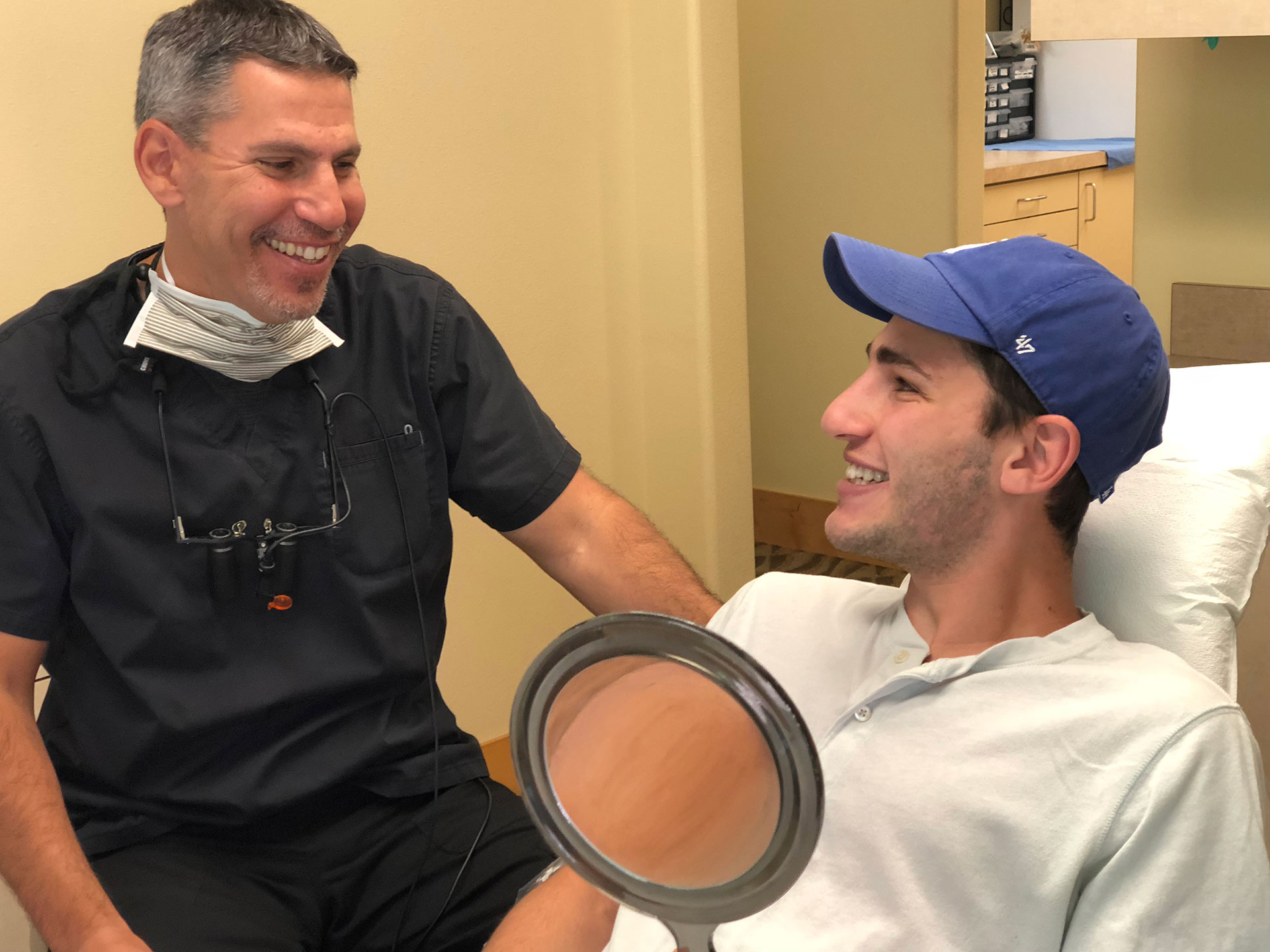 A dentist and patient in a dental office, with the dentist smiling at the camera.