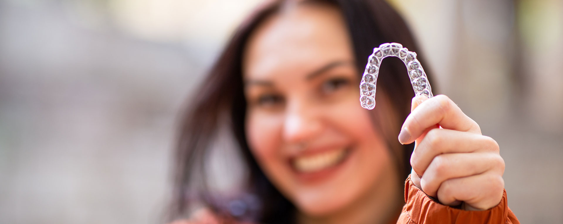 A smiling woman holding a toothbrush with a smiley face on it.