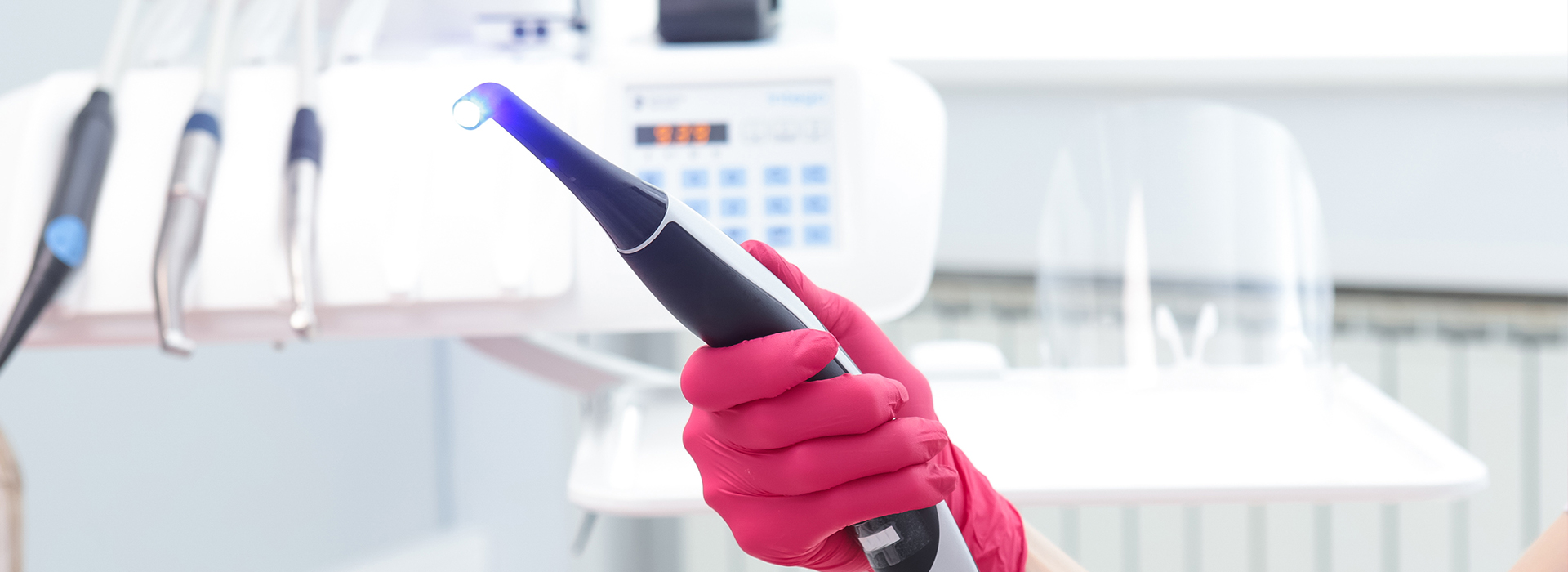 The image shows a person wearing pink gloves and holding a blue device, possibly an ultrasonic cleaning tool, in front of a white background with various items that could be laboratory equipment.
