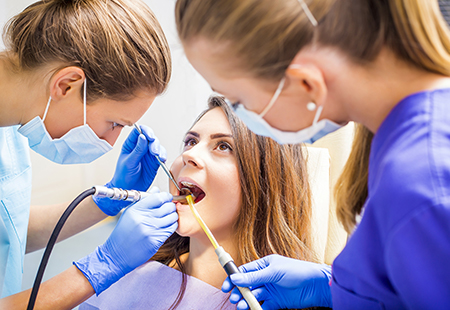 A dental hygienist assisting a patient in a dental chair during a teeth cleaning appointment.