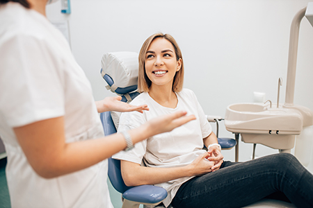 The image shows a dental professional assisting a seated patient in what appears to be a dental office, with both individuals smiling and engaged in conversation.