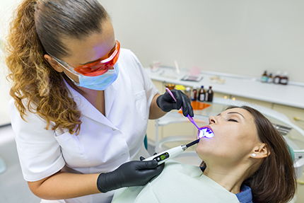 A dental hygienist performing oral care procedures, with a patient seated in the chair receiving treatment.