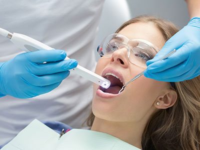 A woman receiving dental treatment, with a dental professional using a laser device to clean her teeth.